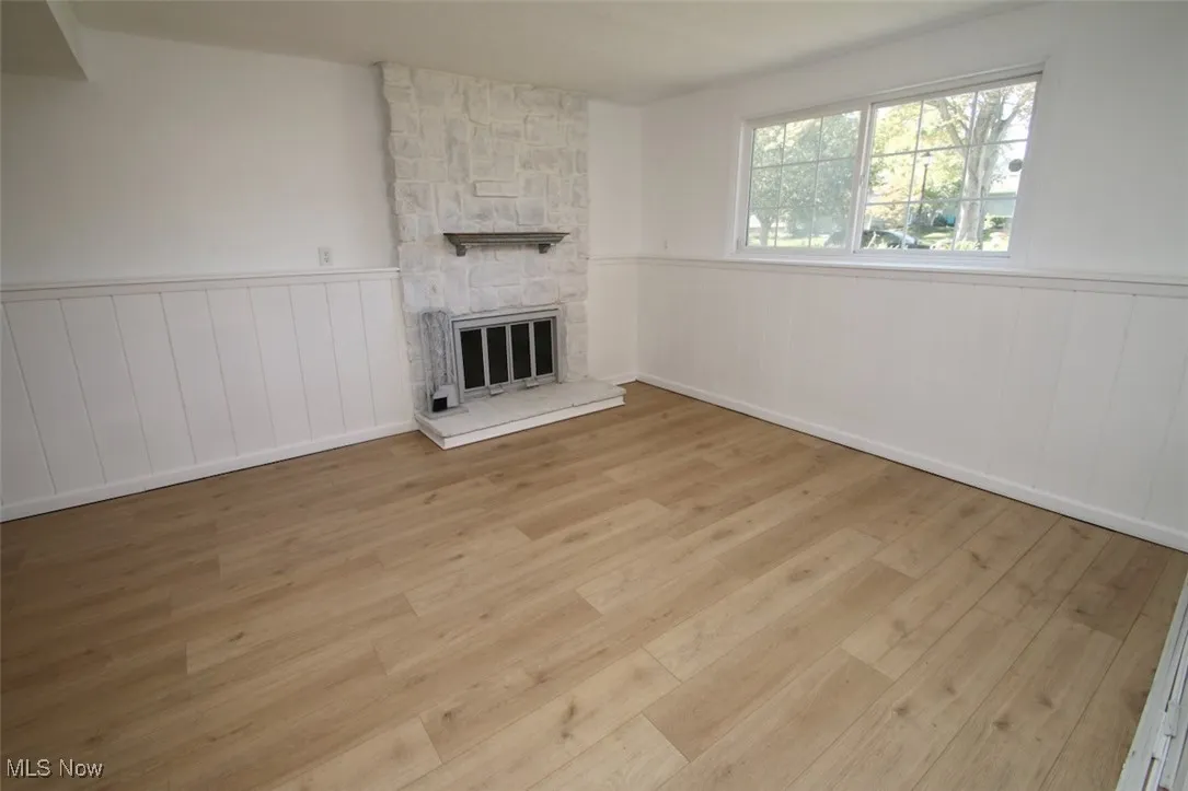 Unfurnished living room featuring wainscoting, a fireplace, and light wood-style flooring