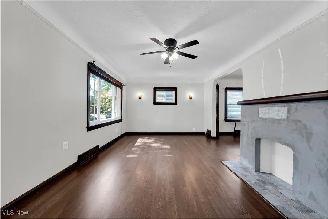 Unfurnished living room with dark wood finished floors, healthy amount of natural light, and a ceiling fan