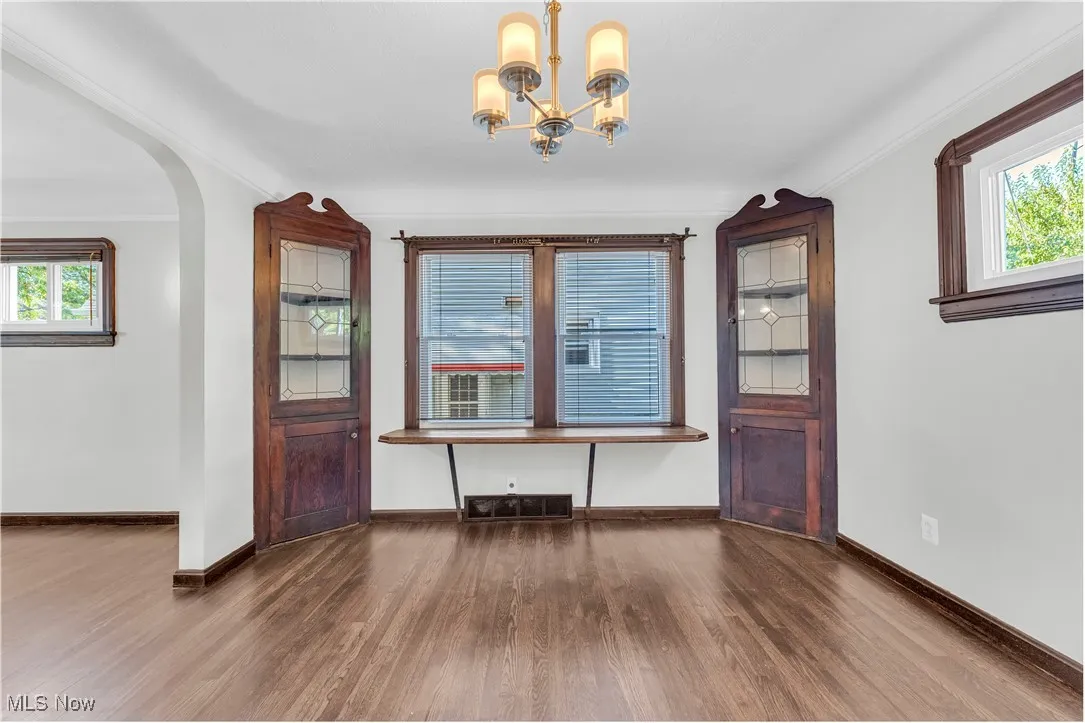 Unfurnished dining area featuring healthy amount of natural light, dark wood-type flooring, crown molding, a chandelier, and arched walkways