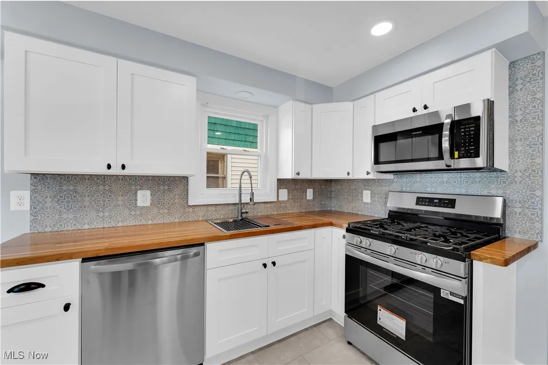 Kitchen featuring butcher block countertops, appliances with stainless steel finishes, white cabinetry, decorative backsplash, and light tile patterned flooring