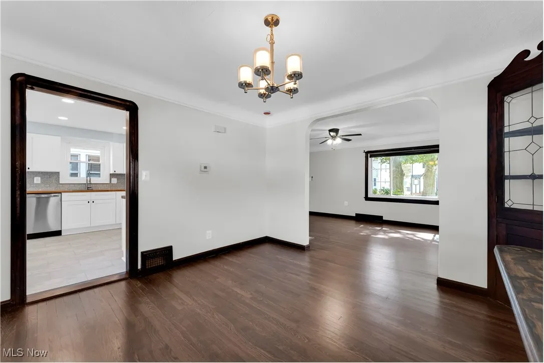 Unfurnished dining area featuring dark wood finished floors, ceiling fan, a chandelier, ornamental molding, and arched walkways