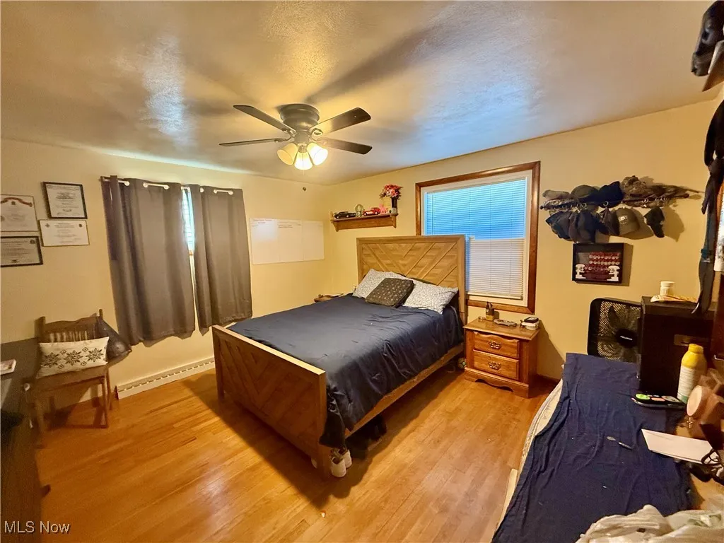 Bedroom featuring wood finished floors, a ceiling fan, a textured ceiling, and baseboard heating