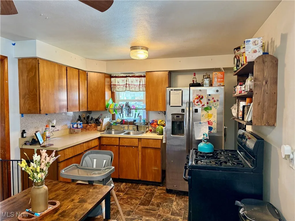 Kitchen featuring black range with gas cooktop, light countertops, brown cabinets, stainless steel fridge, and stone finish floors
