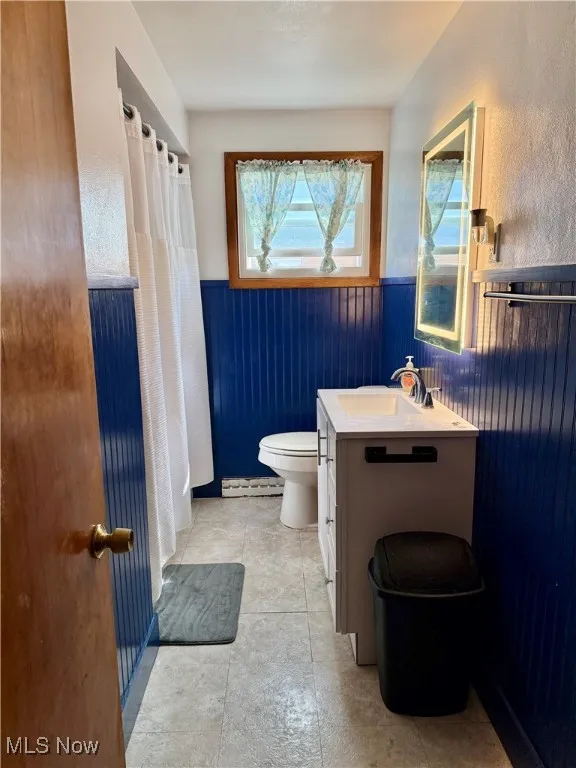 Full bathroom featuring vanity, wainscoting, wood walls, a shower with curtain, and a baseboard radiator