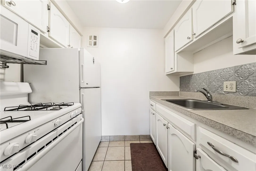Kitchen featuring white appliances, white cabinetry, light tile patterned flooring, and backsplash