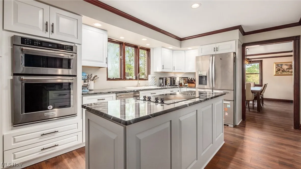 Kitchen featuring white cabinets, ornamental molding, appliances with stainless steel finishes, dark stone countertops, and plenty of natural light