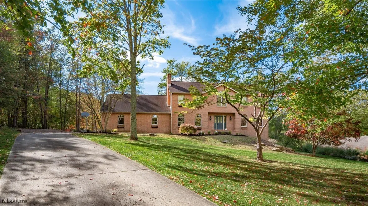 Traditional-style home featuring a front lawn, a chimney, driveway, and brick siding