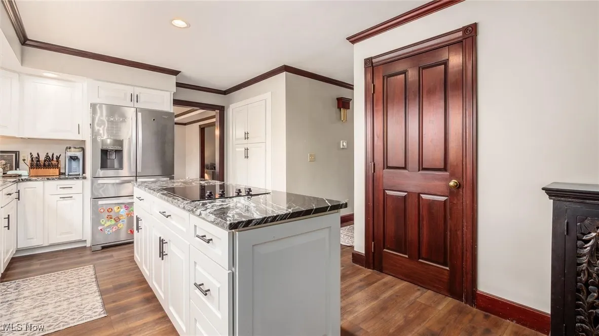 Kitchen with stainless steel fridge, a kitchen island, white cabinets, ornamental molding, and recessed lighting