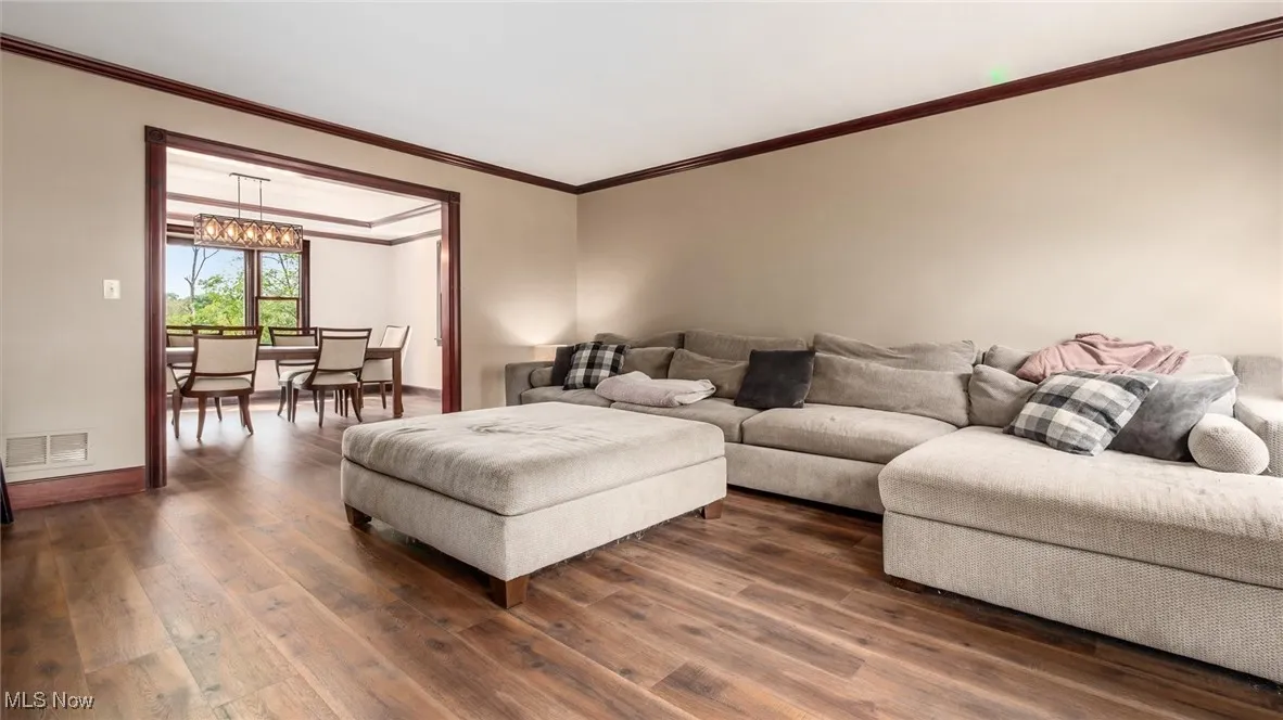 Living room with ornamental molding, wood finished floors, and a chandelier