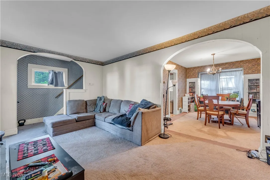 Carpeted living room featuring healthy amount of natural light, arched walkways, wallpapered walls, and a chandelier