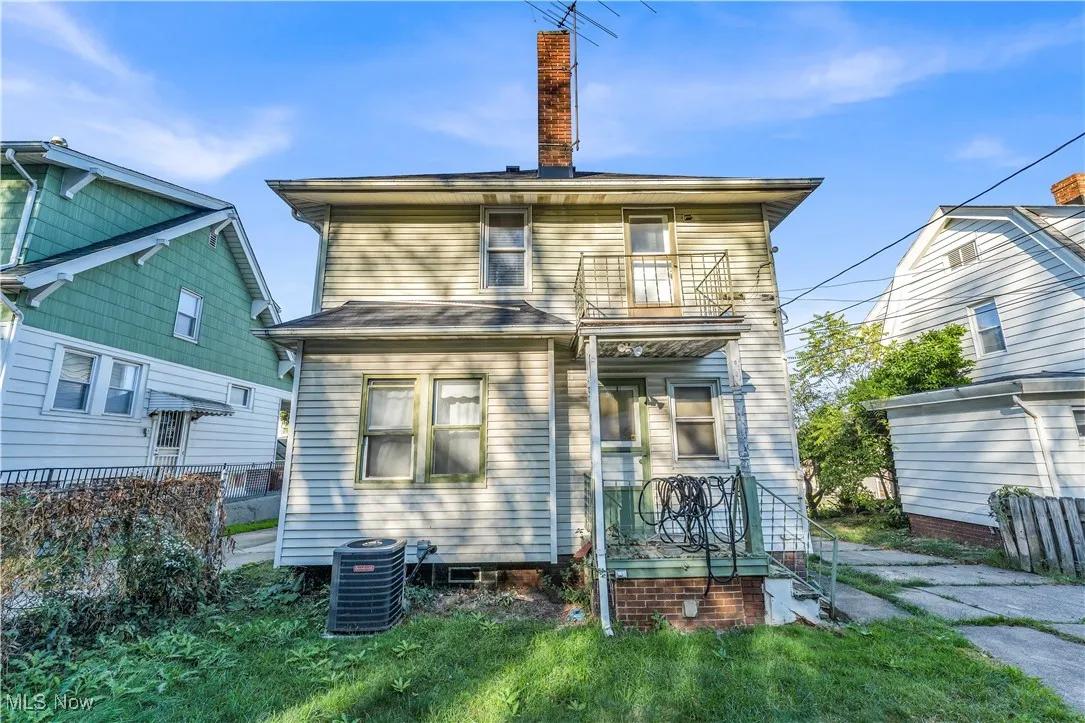 Rear view of property featuring a chimney, a balcony, and a lawn