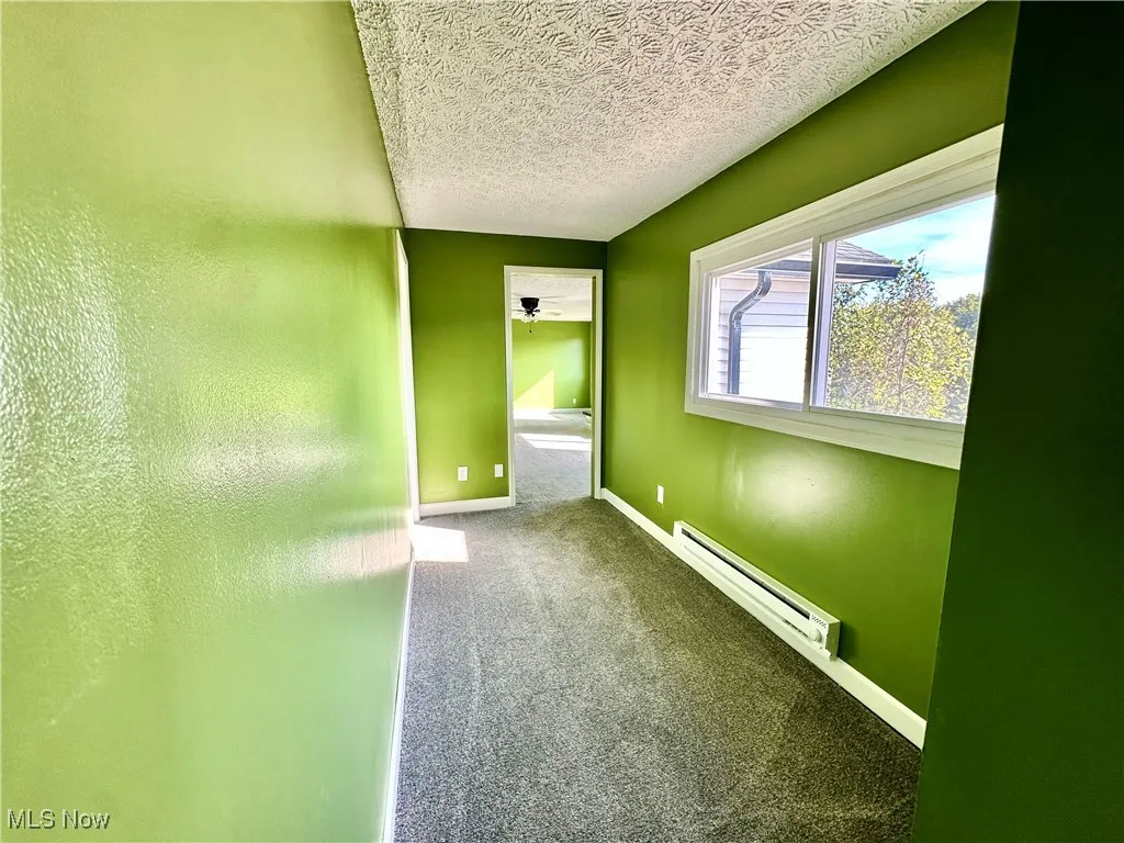 Carpeted spare room featuring a baseboard heating unit, a textured ceiling, and ceiling fan