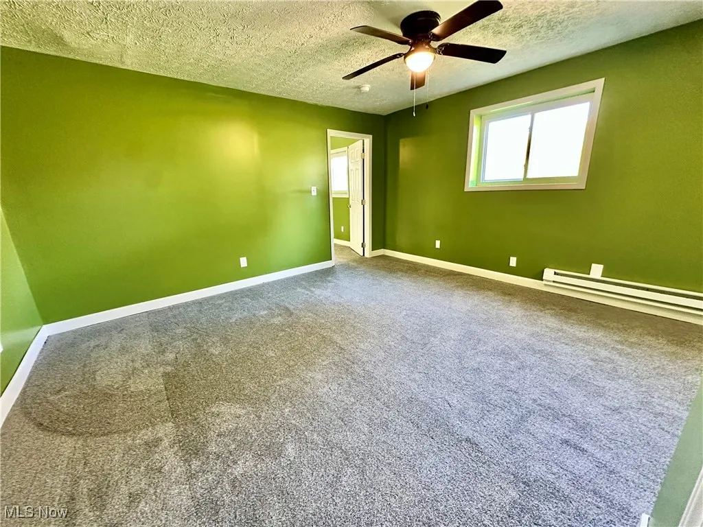 Carpeted empty room with a textured ceiling, a baseboard heating unit, and ceiling fan