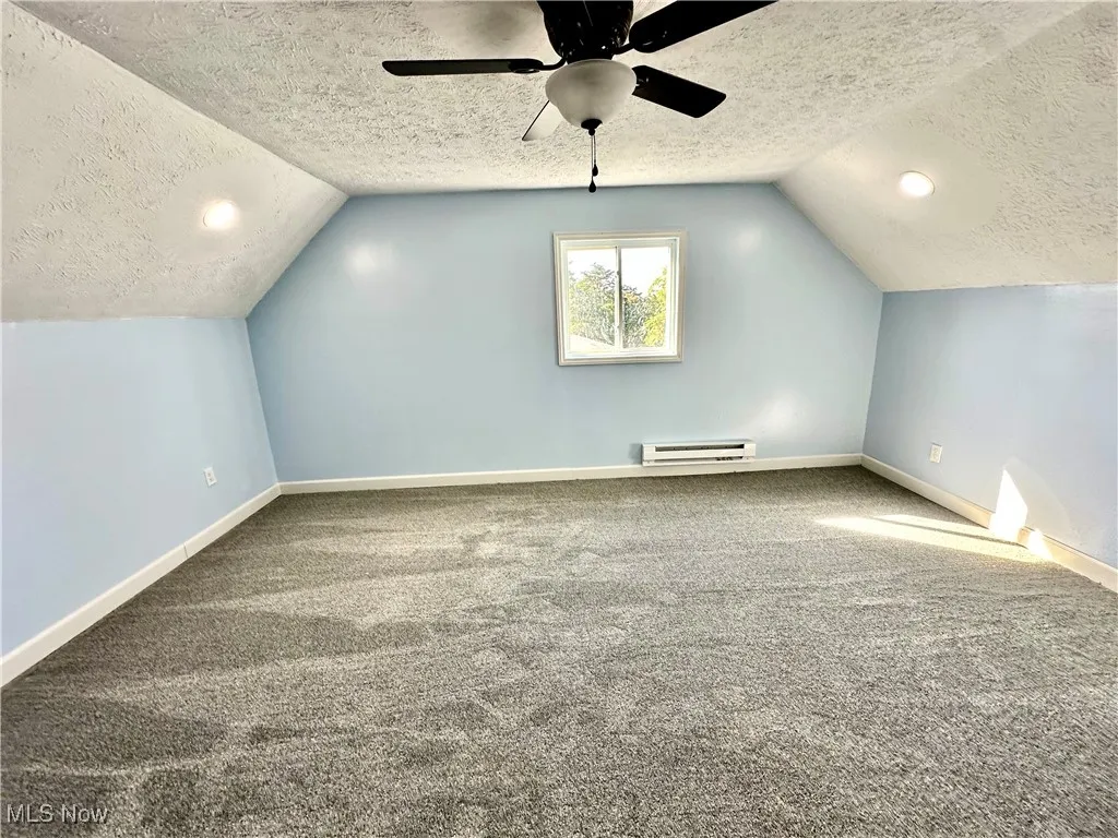 Bonus room featuring a textured ceiling, lofted ceiling, carpet flooring, a baseboard radiator, and a ceiling fan
