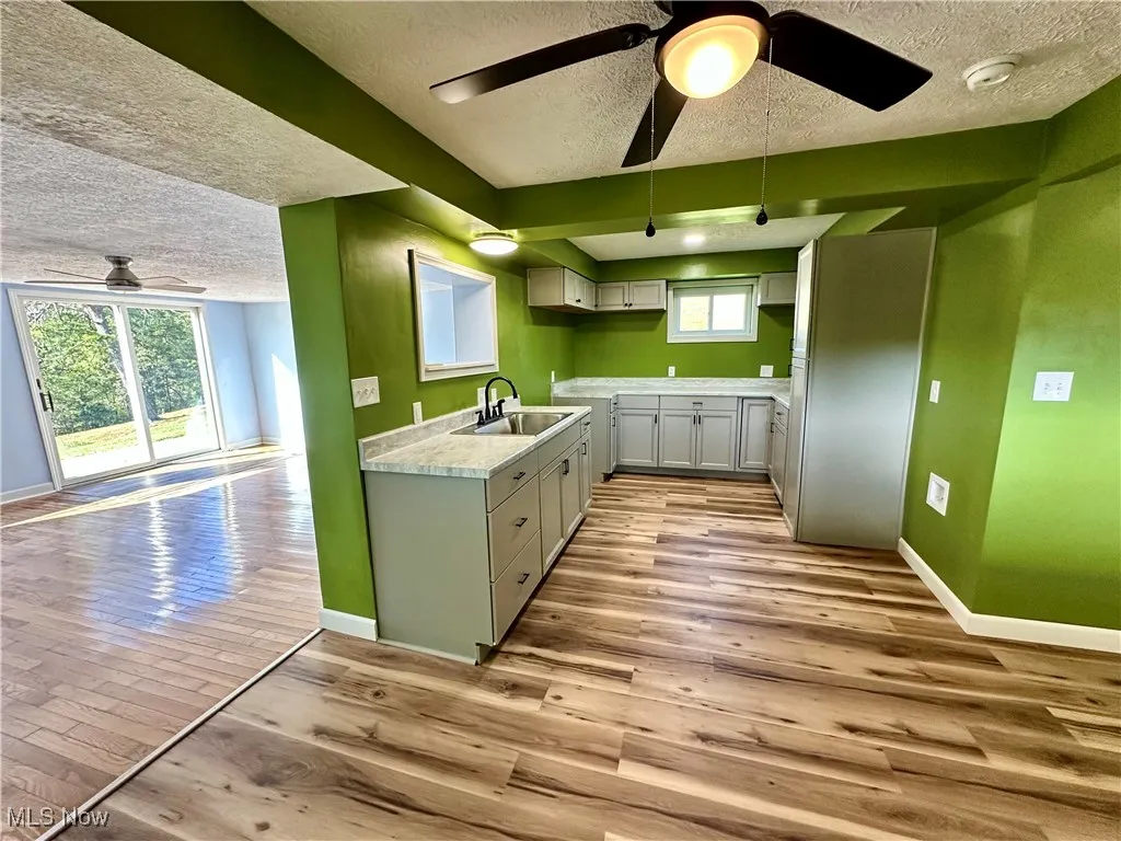 Kitchen featuring a ceiling fan, a textured ceiling, light countertops, light wood-type flooring, and open floor plan