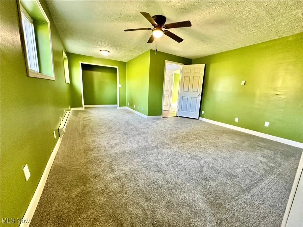 Unfurnished bedroom with carpet, a textured ceiling, a ceiling fan, and baseboard heating