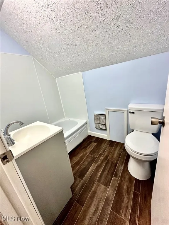 Full bath with wood finish floors, vanity, a textured ceiling, heating unit, and a bath