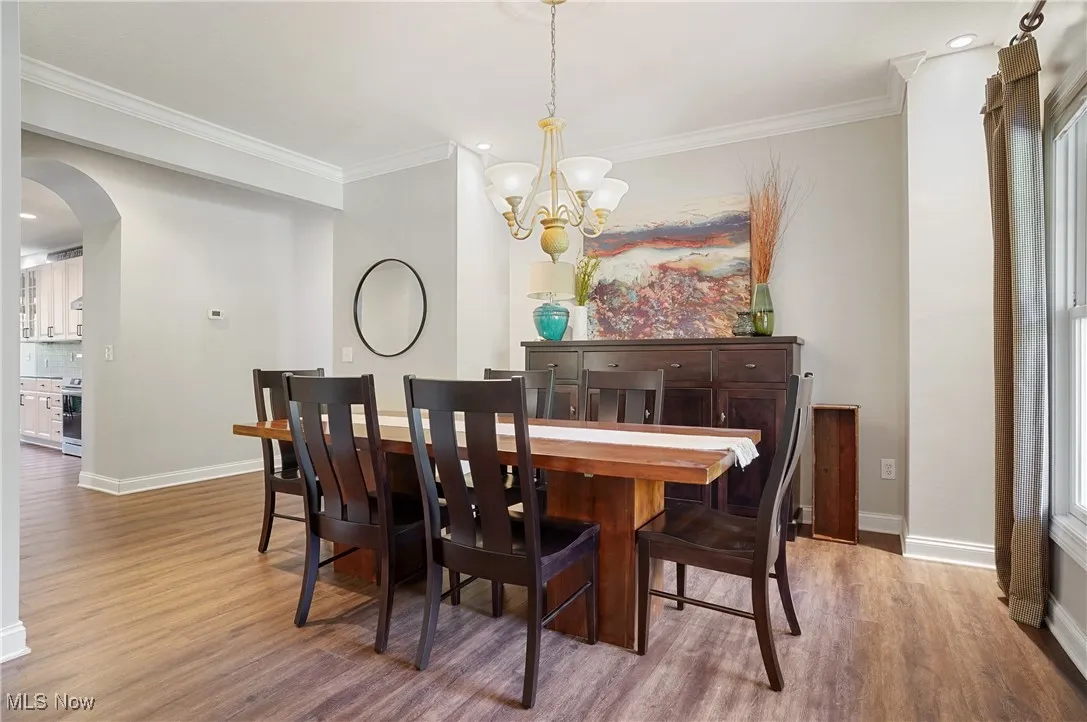 Dining room featuring arched walkways, crown molding, light wood-type flooring, recessed lighting, and a chandelier