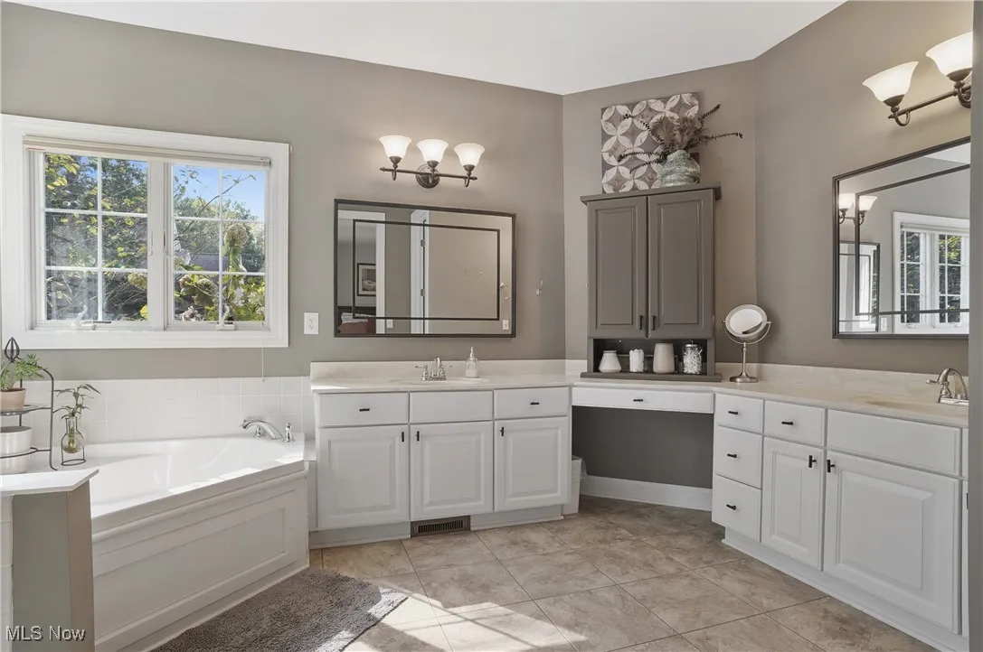 Bathroom featuring two vanities, a bath, and light tile patterned flooring