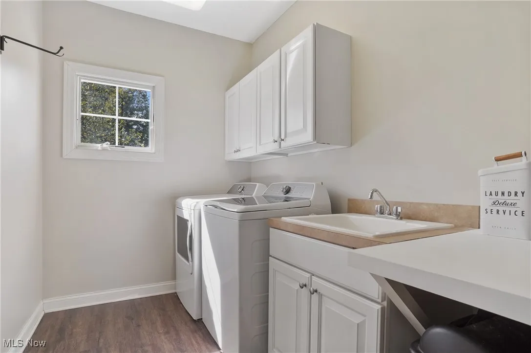 Washroom with dark wood-type flooring, washing machine and clothes dryer, and cabinet space