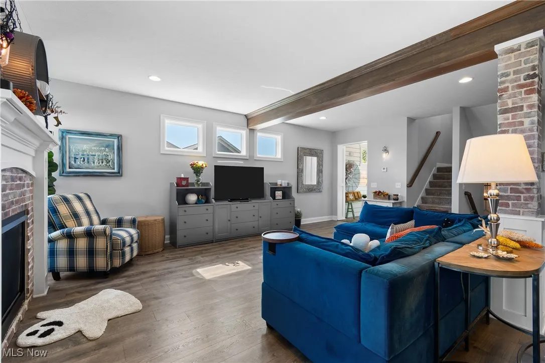 Living room featuring beam ceiling, a fireplace, wood finished floors, recessed lighting, and stairway