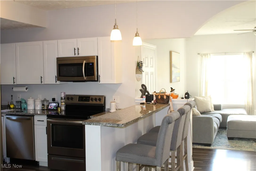 Kitchen with stainless steel appliances, a breakfast bar, dark stone counters, open floor plan, and arched walkways