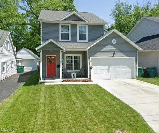 View of front of property with covered porch, driveway, a front yard, a garage, and roof with shingles