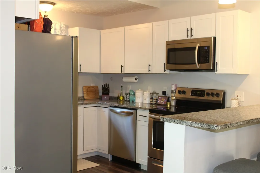 Kitchen featuring stainless steel appliances, light stone counters, white cabinets, and a textured ceiling