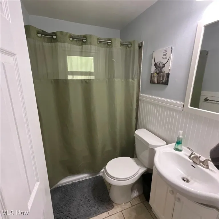 Full bath with vanity, light tile patterned flooring, and a wainscoted wall