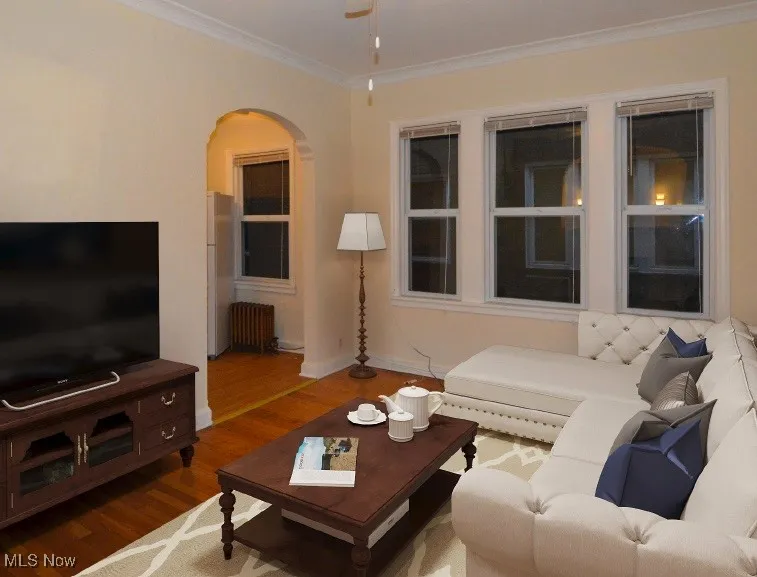 Virtually Staged Living area with ornamental molding, wood finished floors, arched walkways, and radiator