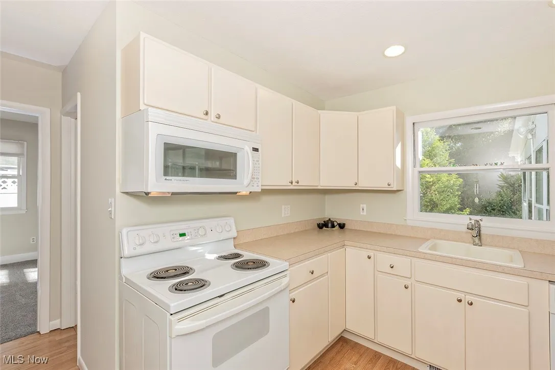 Kitchen featuring white appliances, light wood-type flooring, light countertops, white cabinetry, and recessed lighting