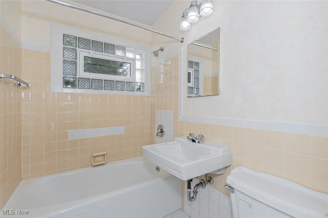 Full bath featuring tub / shower combination, tile walls, and a wainscoted wall