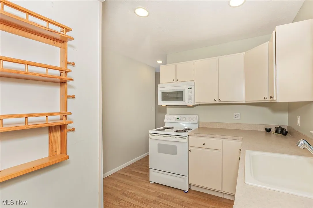 Kitchen with white appliances, light countertops, light wood-type flooring, recessed lighting, and white cabinets