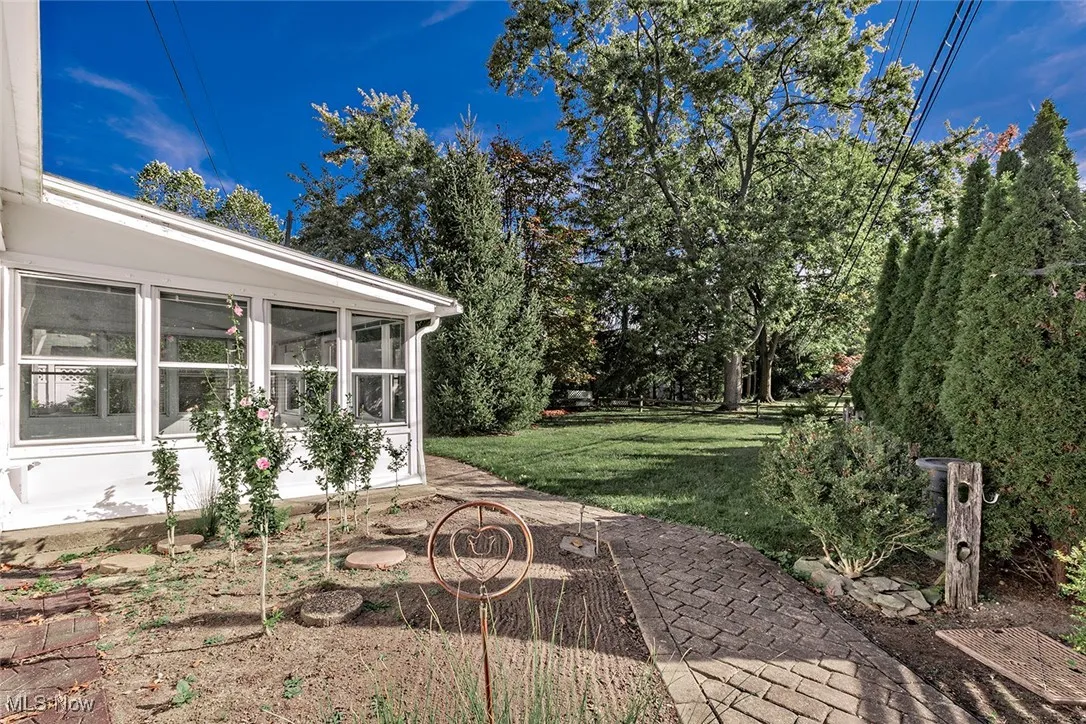 View of grassy yard featuring a sunroom, view of scattered trees, and a patio