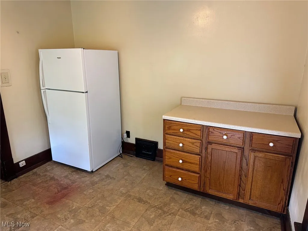 Kitchen with freestanding refrigerator, brown cabinets, and stone finish floors