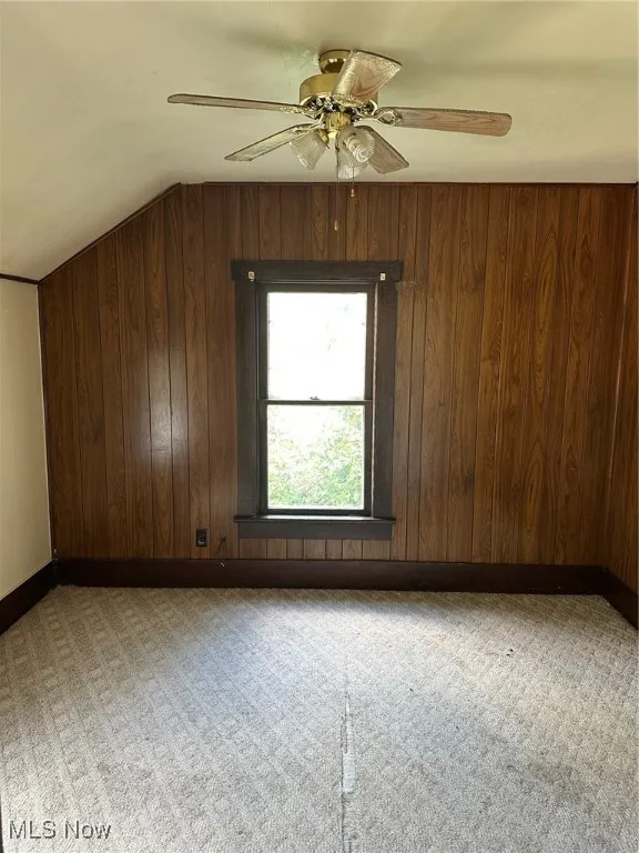 Additional living space featuring wooden walls, a ceiling fan, and light carpet