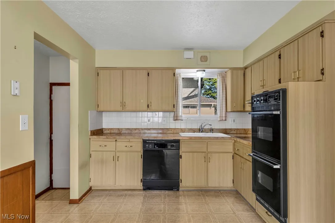 Kitchen with black appliances, light brown cabinetry, backsplash, and light countertops