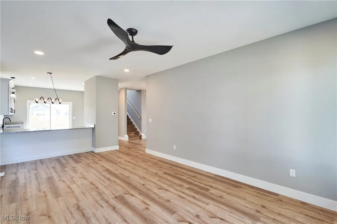 Unfurnished living room featuring sink, light hardwood / wood-style flooring, and ceiling fan with notable chandelier
