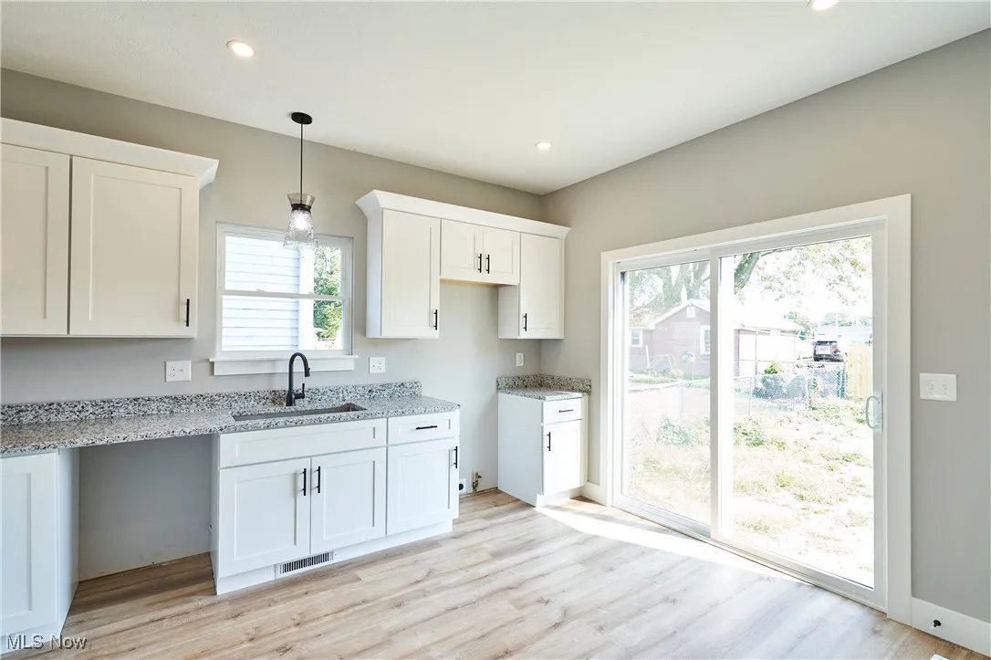 Kitchen with hanging light fixtures, white cabinetry, light stone countertops, light hardwood / wood-style floors, and sink