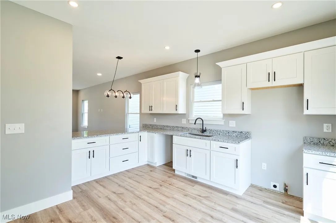 Kitchen featuring sink, white cabinetry, pendant lighting, and light wood-type flooring
