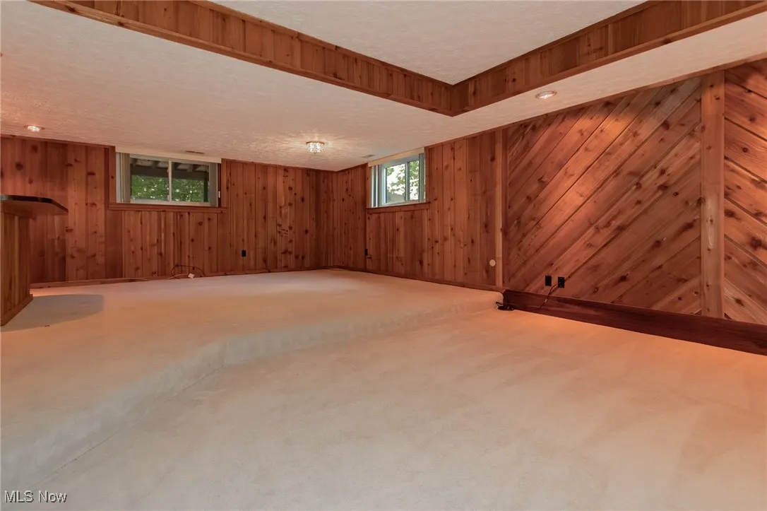 Below grade area featuring a textured ceiling, light colored carpet, wood walls, and recessed lighting