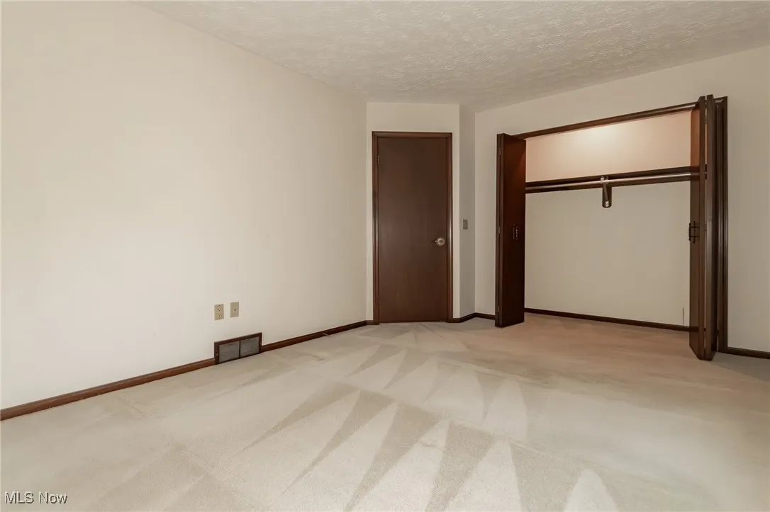 Unfurnished bedroom with a textured ceiling, light colored carpet, and a closet