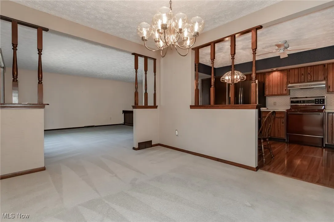 Unfurnished dining area featuring a textured ceiling, dark colored carpet, a chandelier, and ceiling fan
