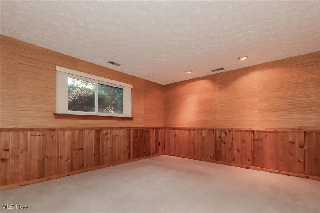 Carpeted spare room featuring wood walls and a textured ceiling
