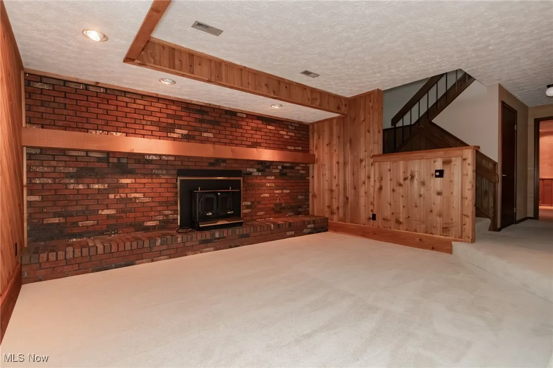 Unfurnished living room with wooden walls, carpet, a textured ceiling, a wood stove, and stairs