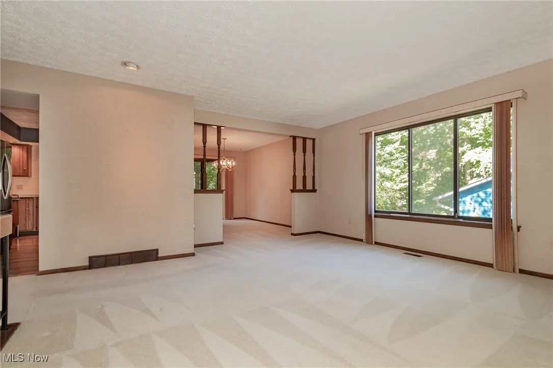 Empty room with light carpet, a textured ceiling, and a chandelier