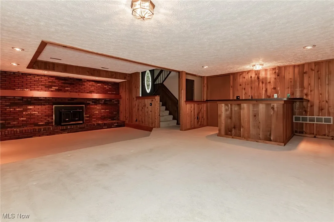 Finished below grade area with a bar, a textured ceiling, light colored carpet, a wood stove, and wood walls