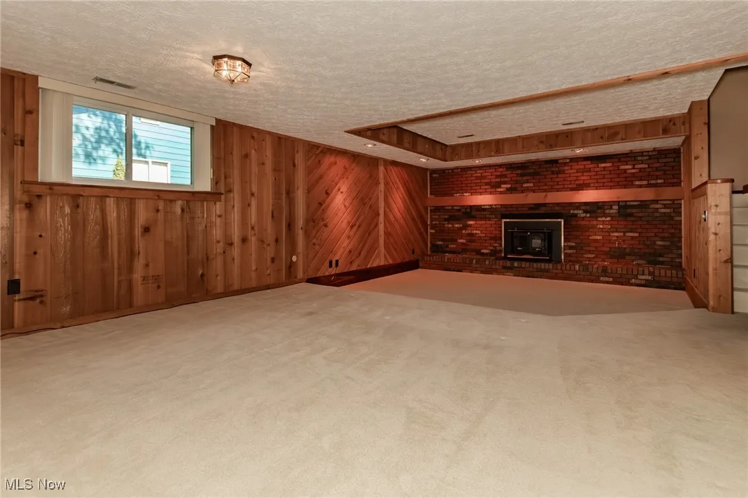 Basement with wooden walls, a textured ceiling, light colored carpet, a fireplace, and brick wall