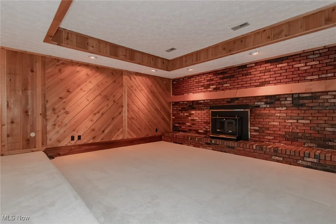Unfurnished living room with a wood stove, a textured ceiling, wooden walls, a raised ceiling, and carpet flooring