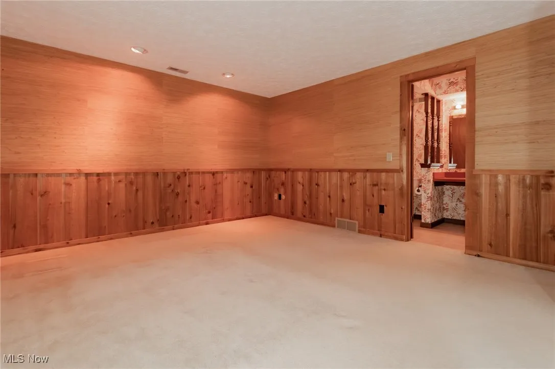 Carpeted spare room featuring a textured ceiling, wooden walls, wainscoting, and recessed lighting